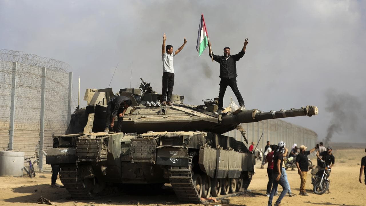 Palestinians wave their national flag on a destroyed Israeli tank