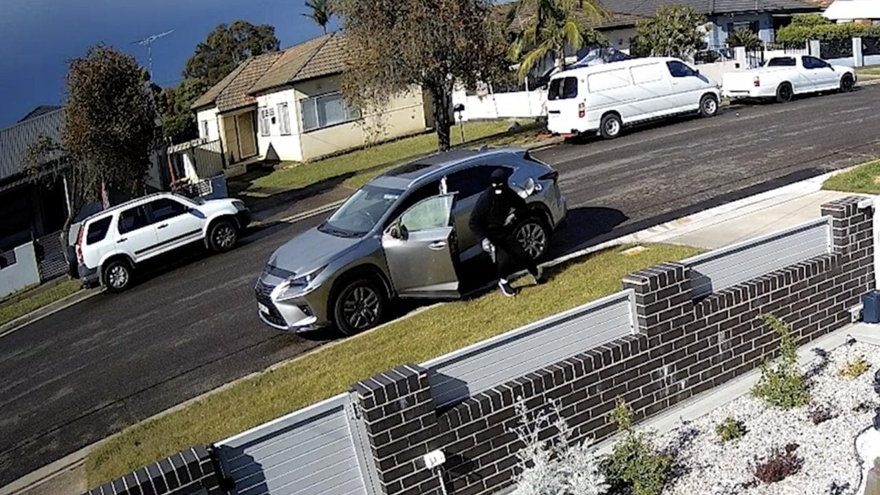 A man wearing a balaclava exits the vehicle and runs toward a ute.