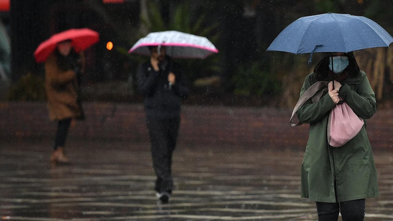 A woman wearing a face mask shelters from the rain