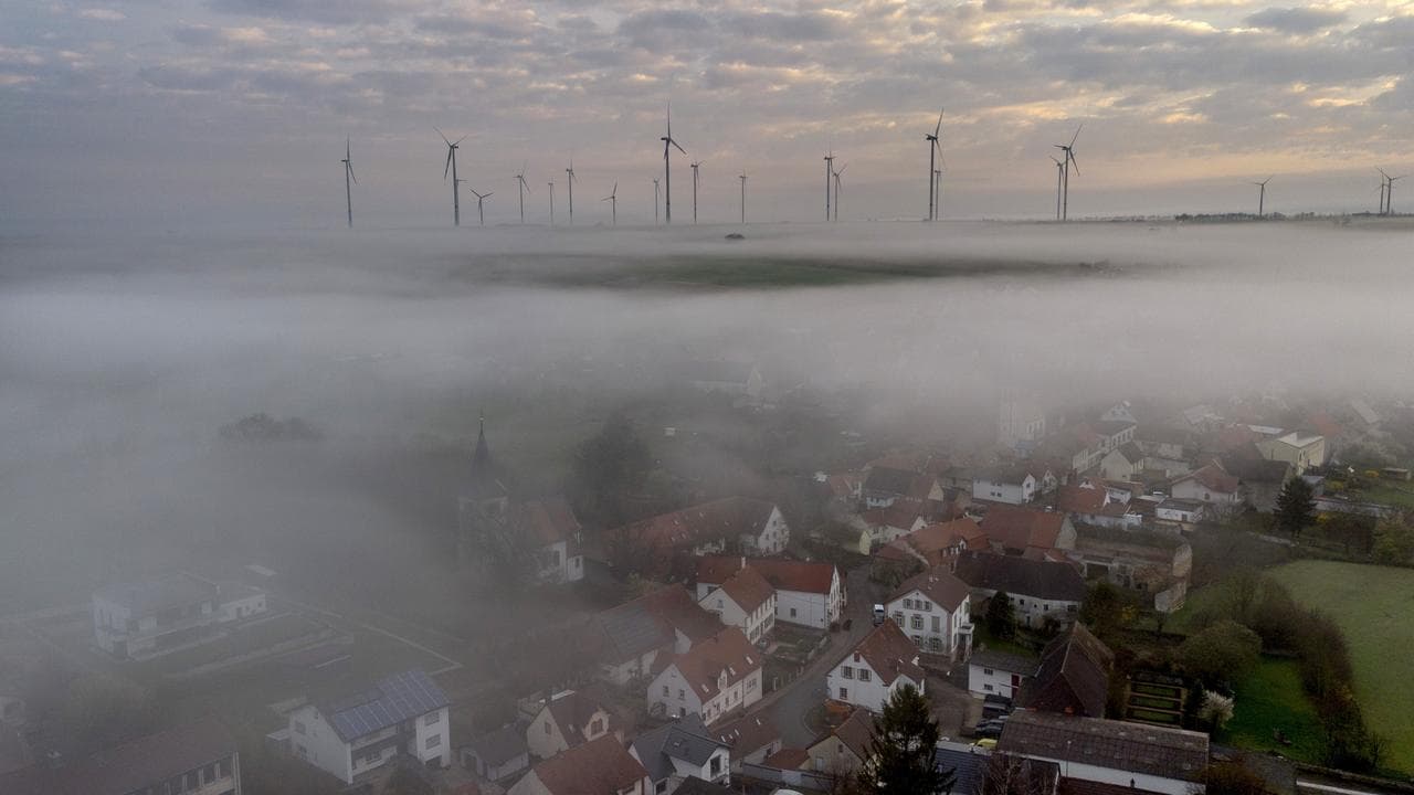 Fog floats over a German village with wind turbine in the background.
