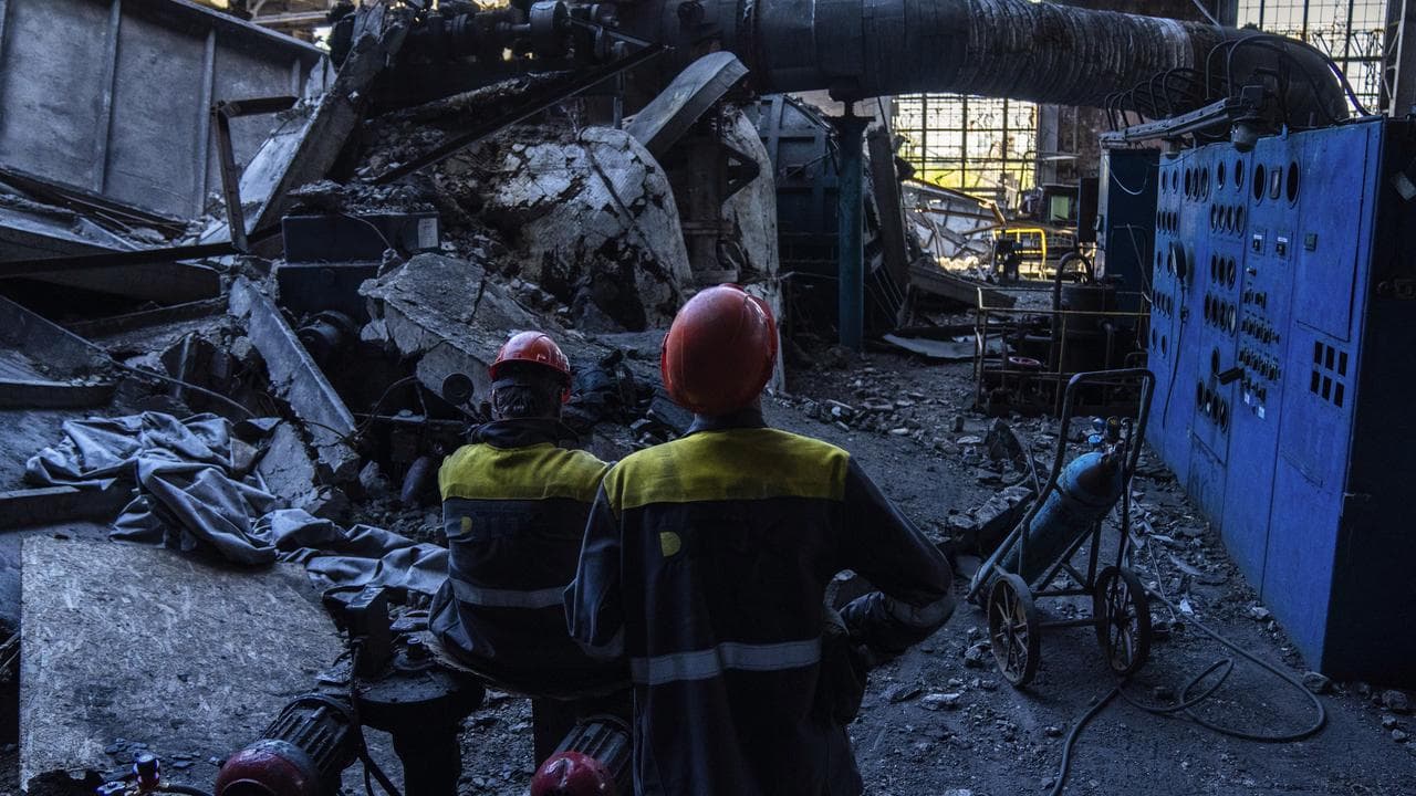 Workers stand among debris in a damaged DTEK thermal power plant