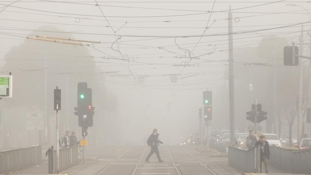 A person crosses a road surrounded by fog.