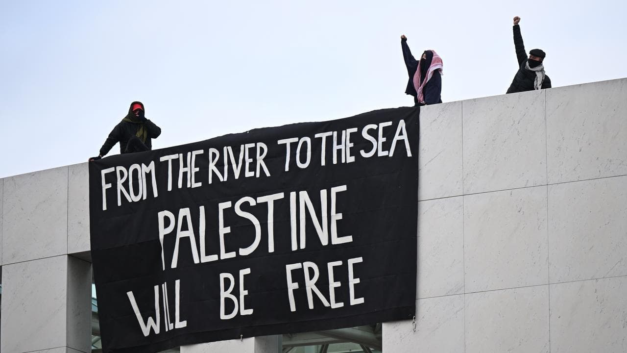 Protesters stand on Parliament House with a banner.