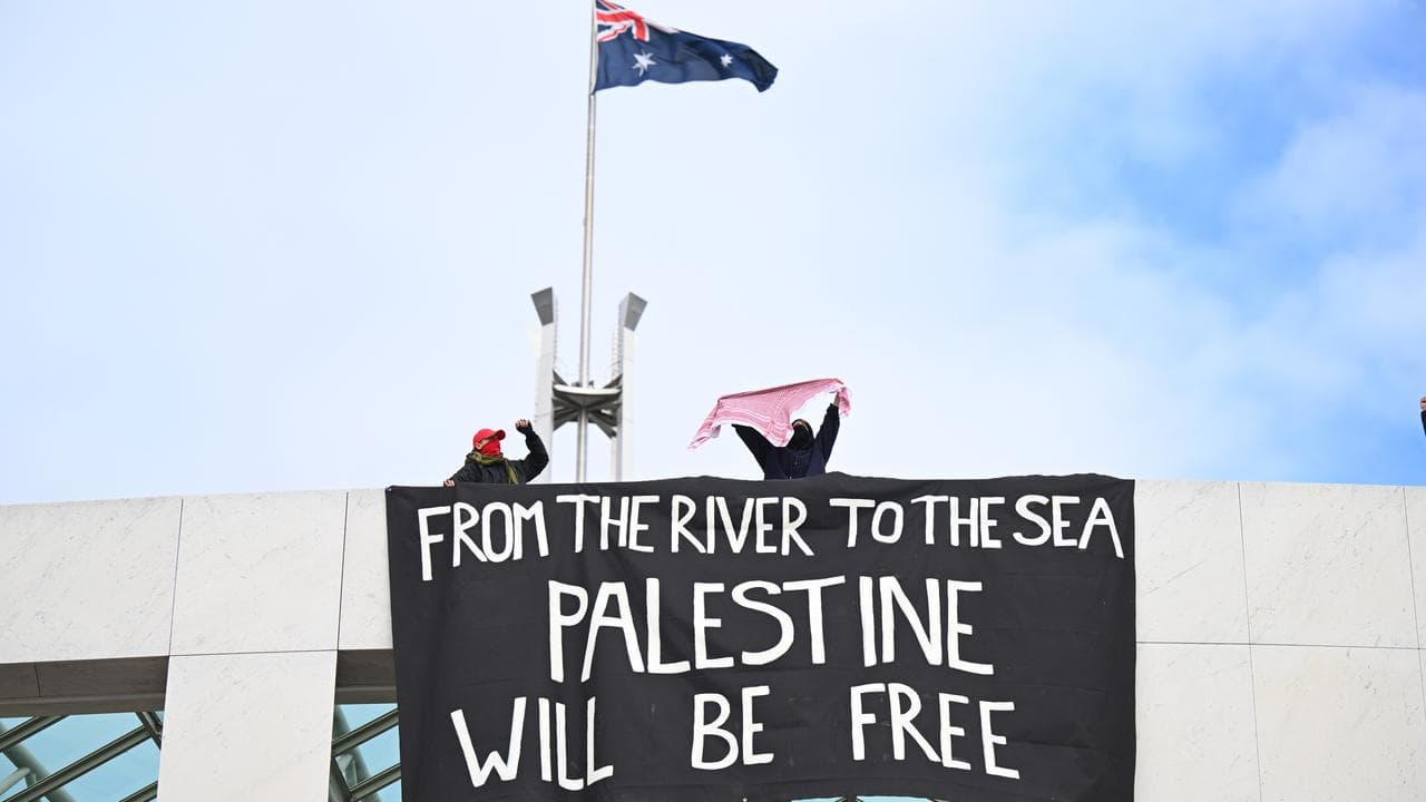 Pro-Palestine protesters hang banners from the top of Parliament House