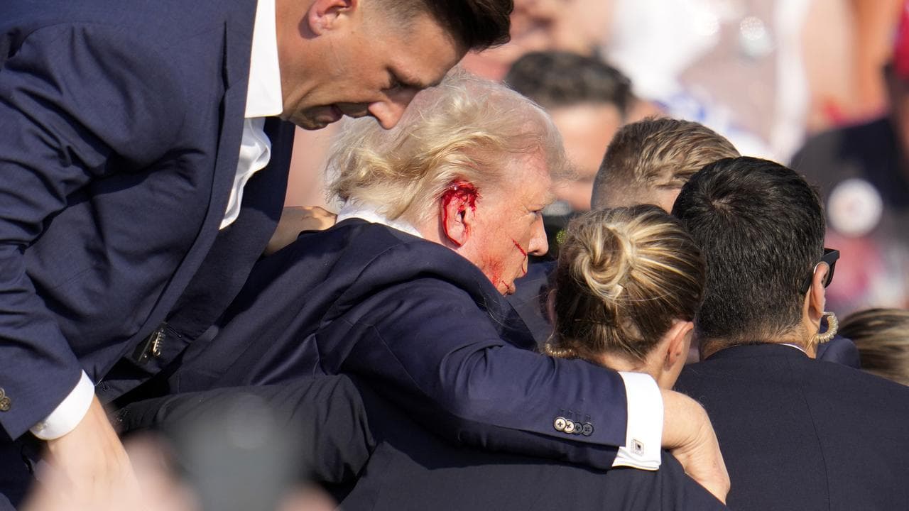 Donald Trump with blood on his ear, being helped off stage