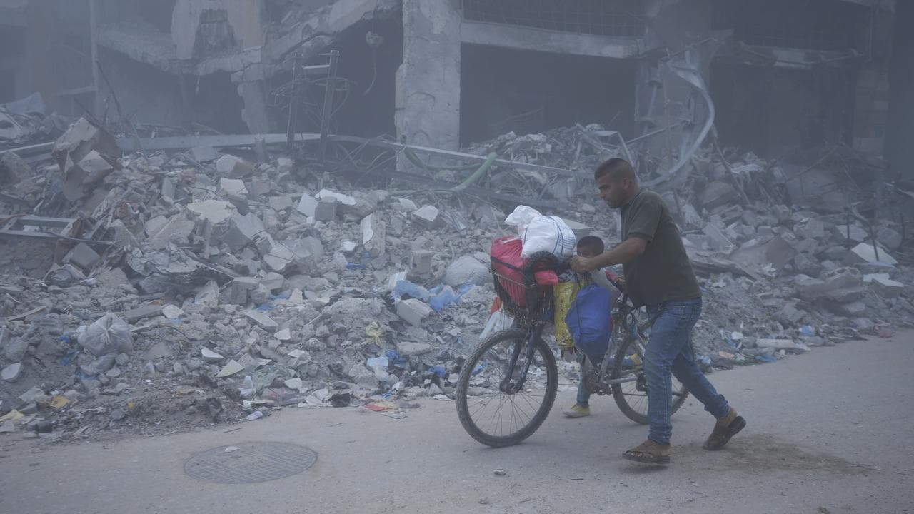 Palestinians walk through dust by the rubble of houses in Khan Younis