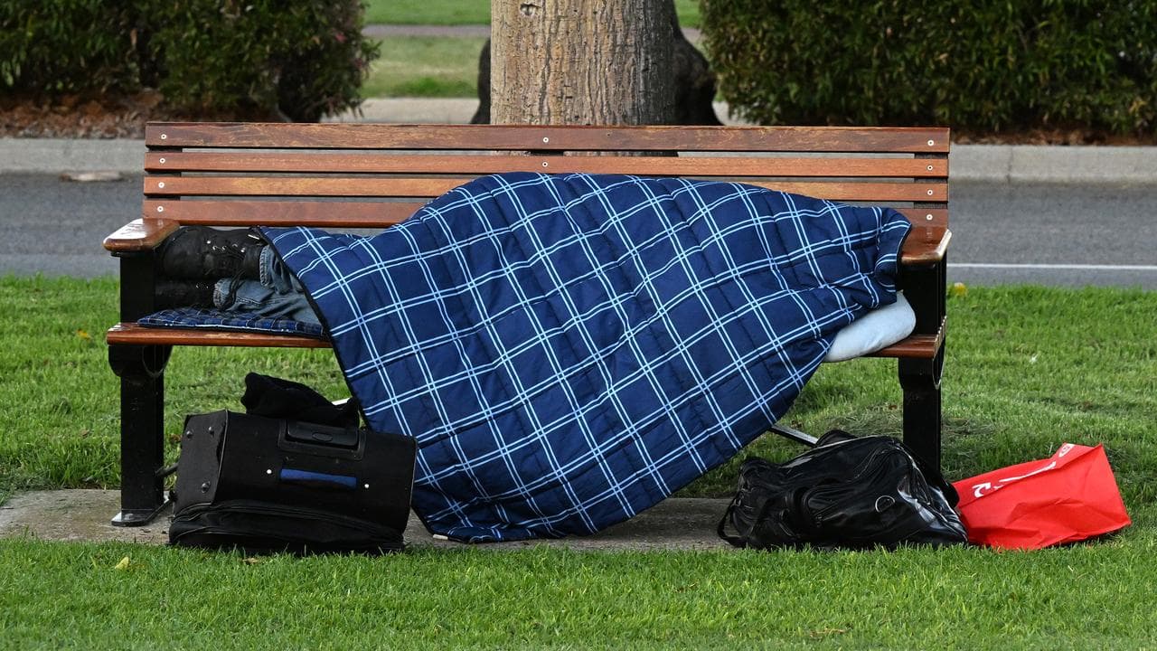 A homeless person sleeps on a park bench.