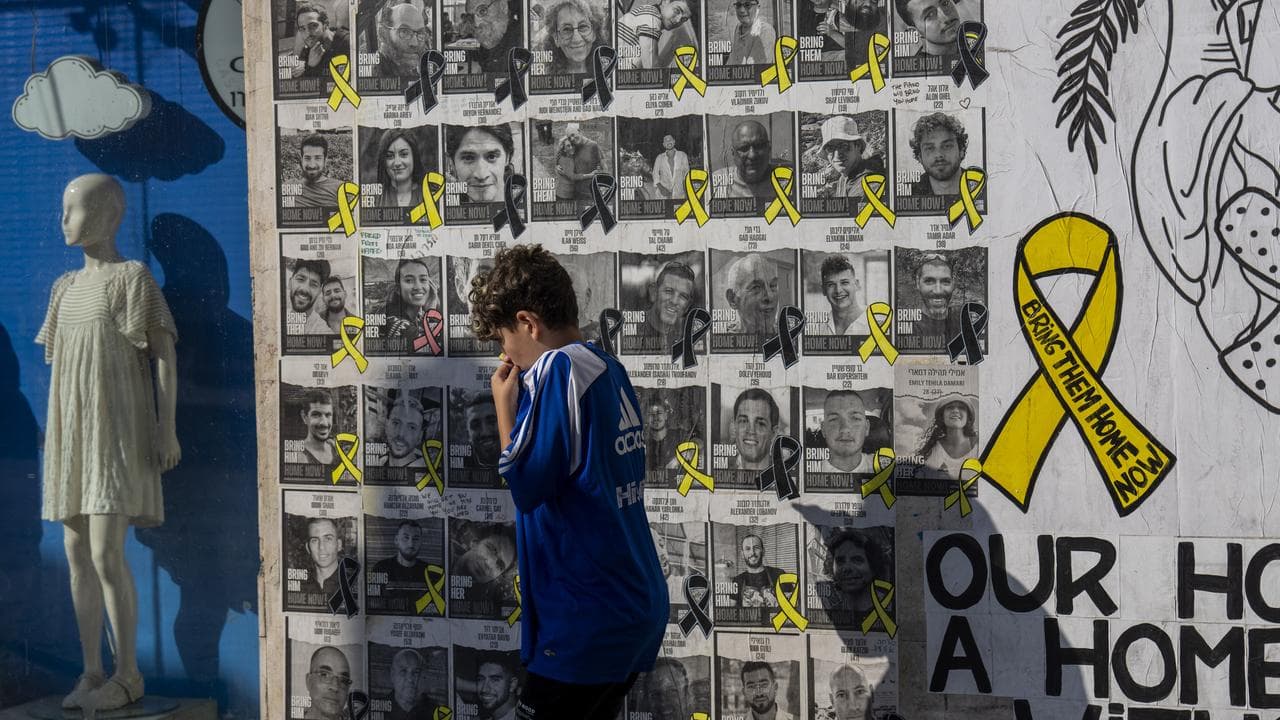 A boy walks past a wall with photos of hostages in Tel Aviv, Israel