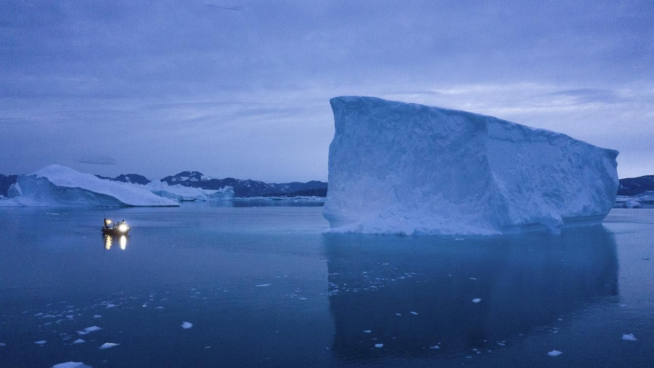 A boat next to large icebergs in Greenland.