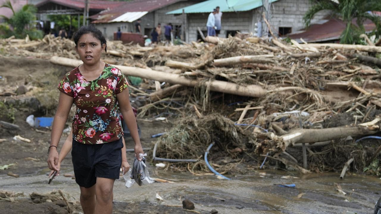 A girl walks past toppled trees