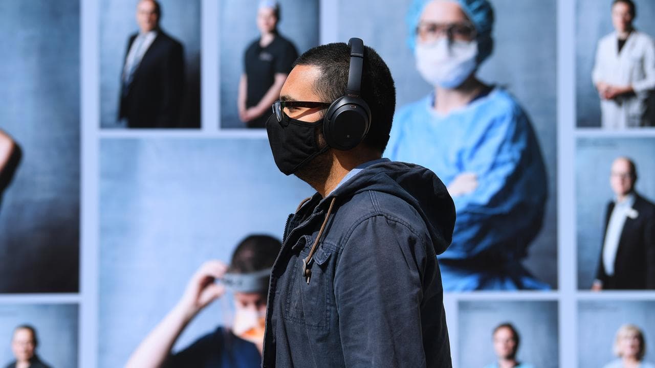 Man in mask walks past photo display of healthcare professionals
