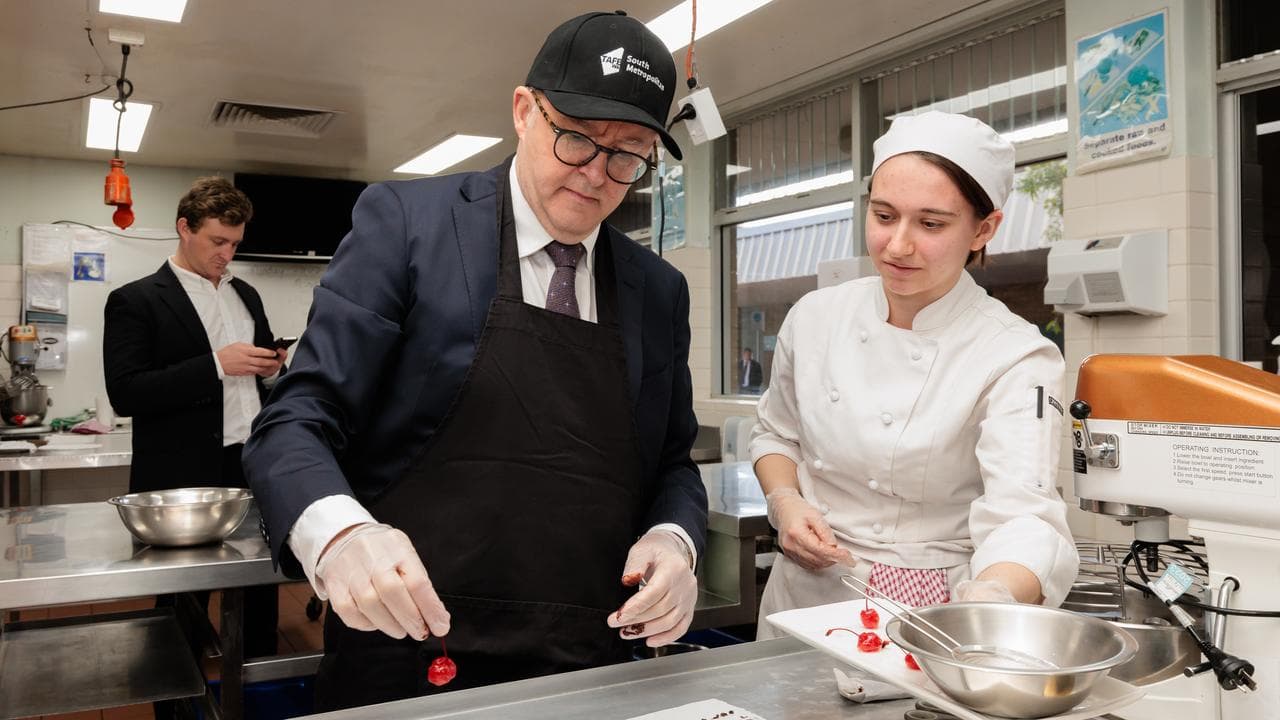 Prime Minister Anthony Albanese decorates a cake with a TAFE student.
