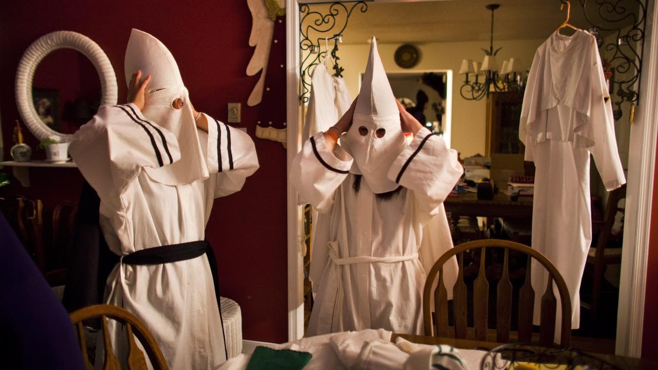 Two Ku Klux Klan members put on robes and hoods.