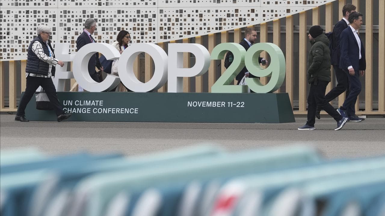 Attendees walk past a sign for the COP29 UN Climate Summit