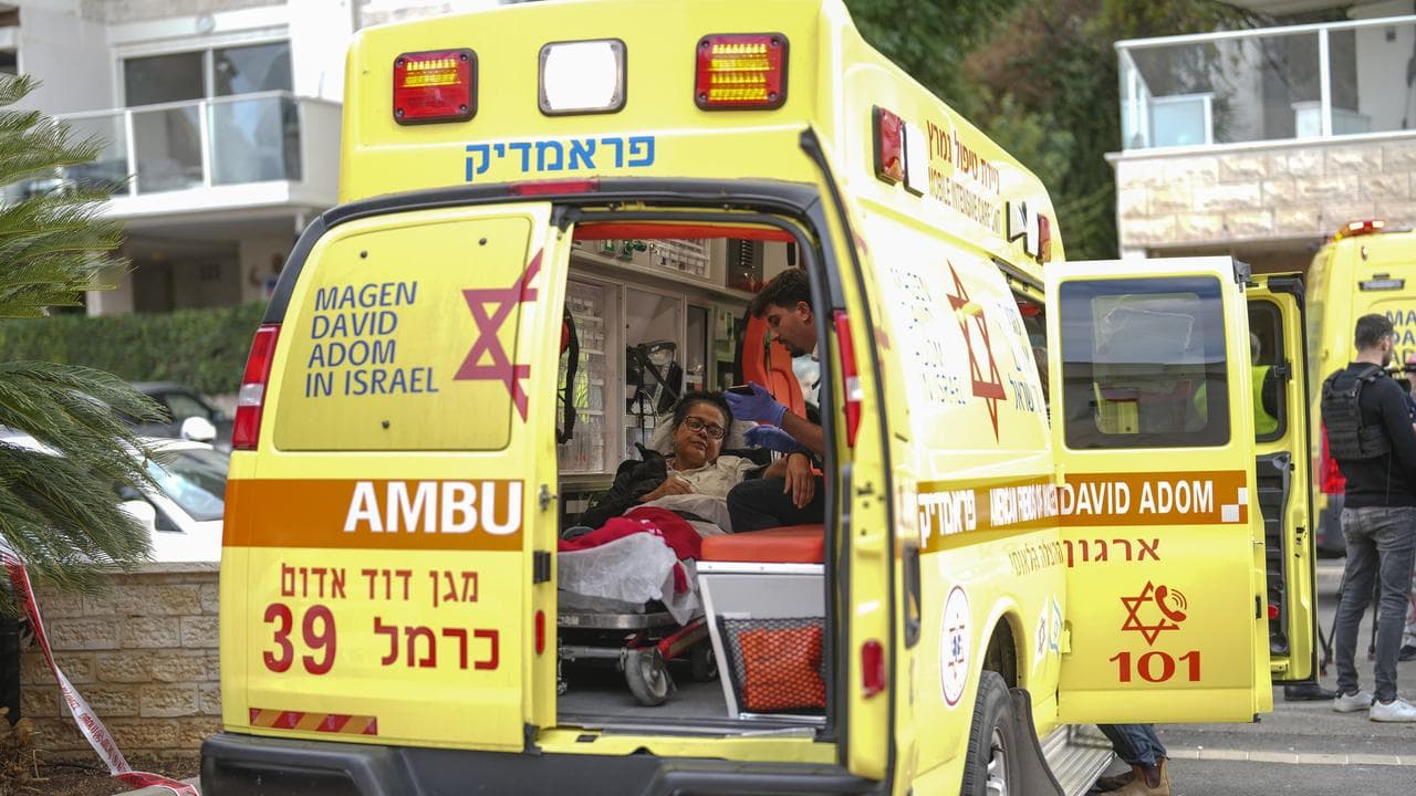 An injured woman in an ambulance near a building hit by a rocket