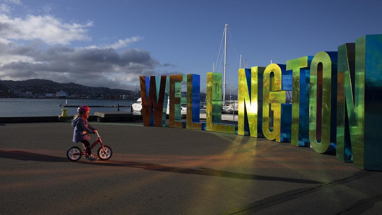 A child on a bicycle stands in front of Wellington sign.