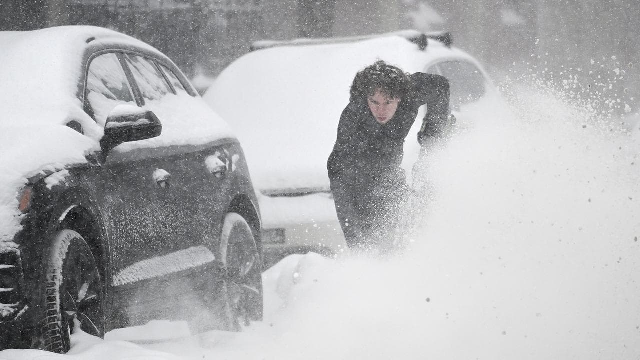 A person clears snow from around a car during a snowstorm