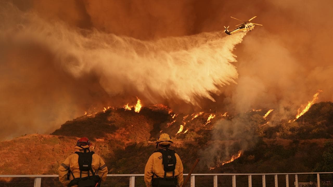 Firefighters watch a helicopter drop water