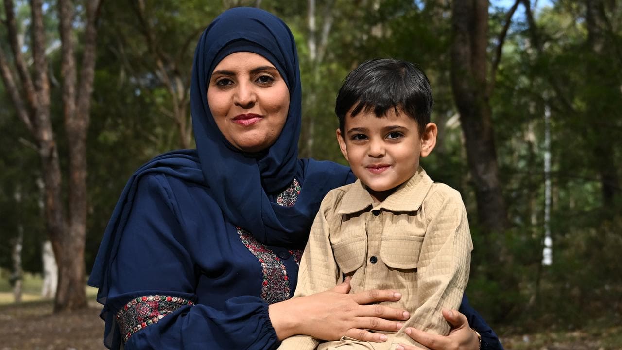 Young boy smiles as he sits on the lap of his mum in a park
