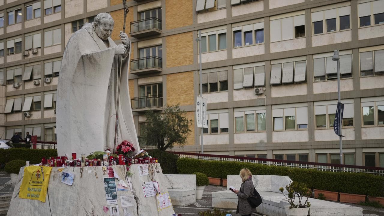 A woman prays at the statue of Pope John Paul II, outside hospital