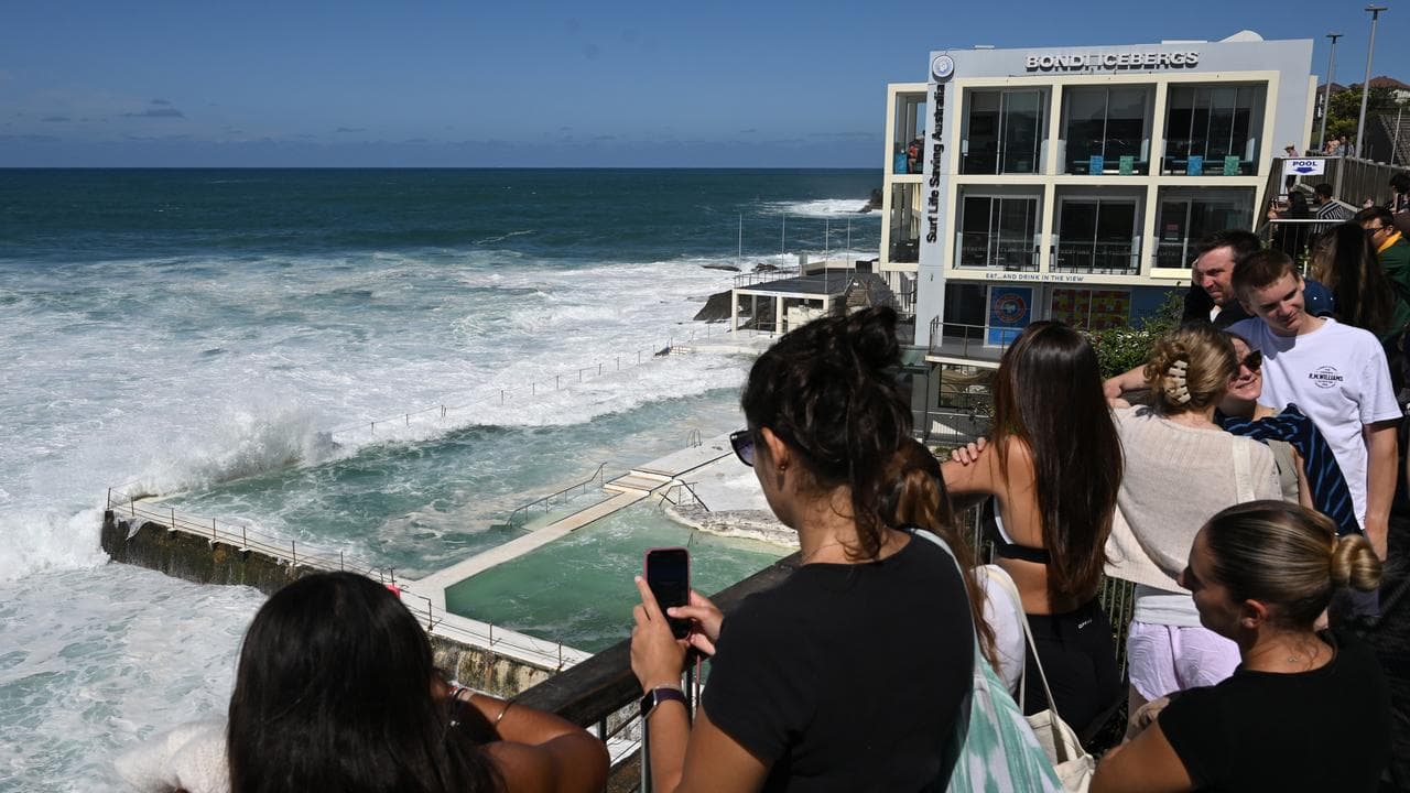 Tourist look on as huge waves pound the Bondi Icebergs