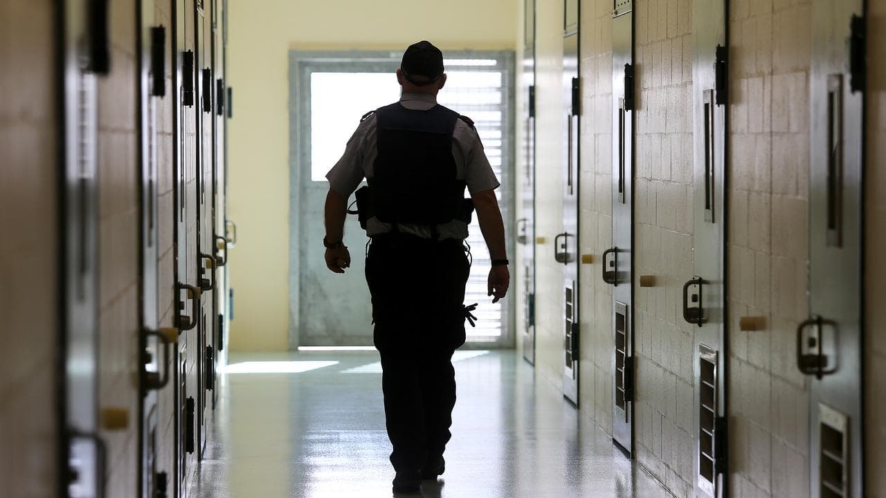 Corrections officers walks down a cell corridor