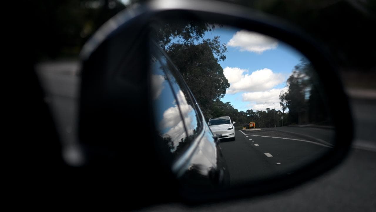 A Tesla is seen in a side mirror of a car in Canberra