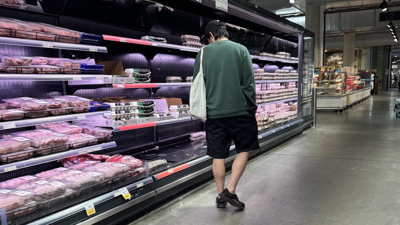 A man walks through the meat aisle in the supermarket.