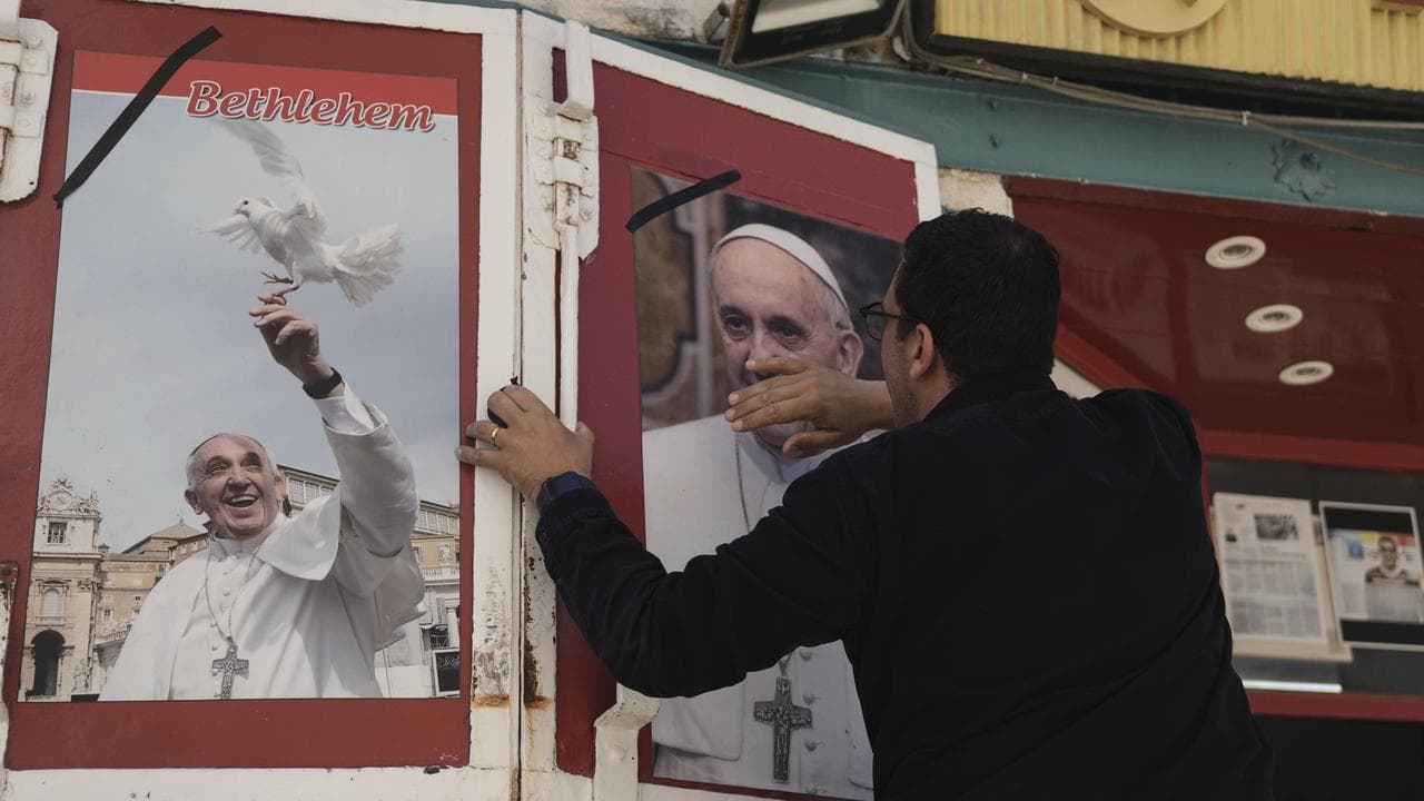 A shop owner places a black ribbon over a photo of Pope Francis