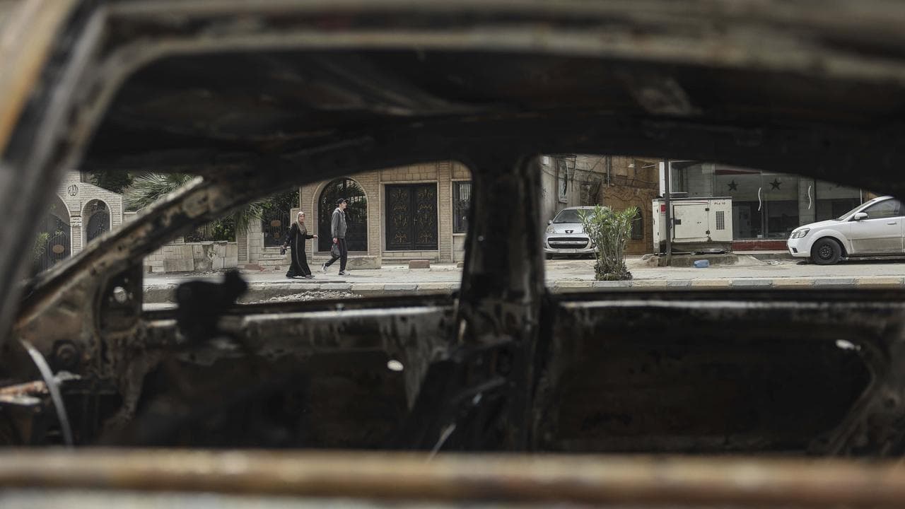 People seen through a car burned during clashes in Damascus
