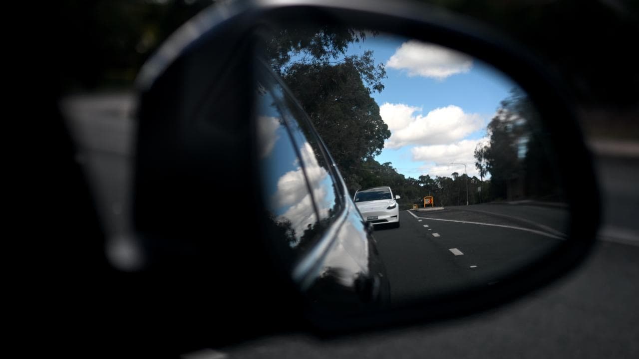 A Tesla is seen in a side mirror of a car in Canberra