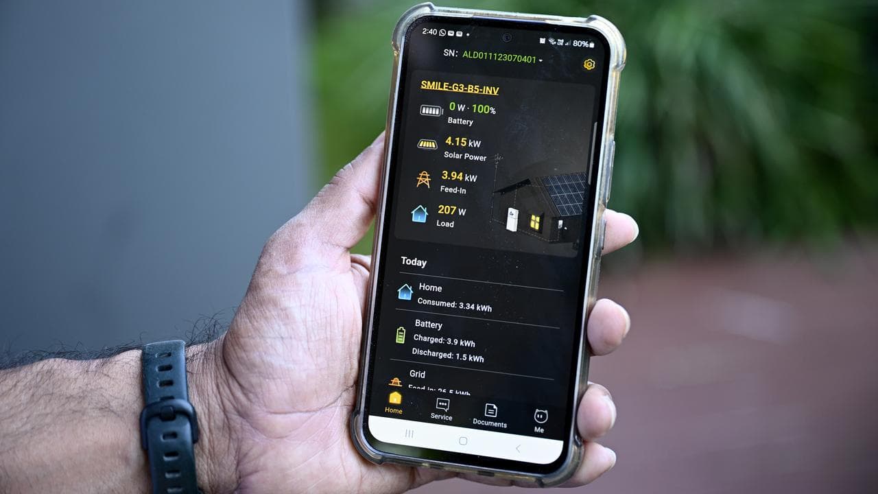 A man holds a smartphone showing details of his solar battery system