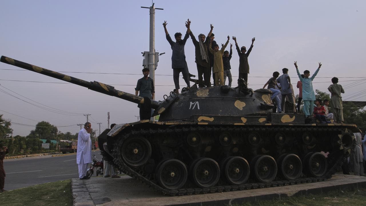 Pakistanis flash victory signs on top of a tank