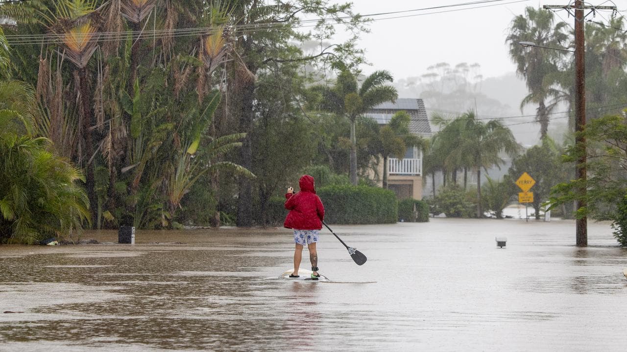 A person uses a paddleboard on a flooded street in Port Macquarie, NSW