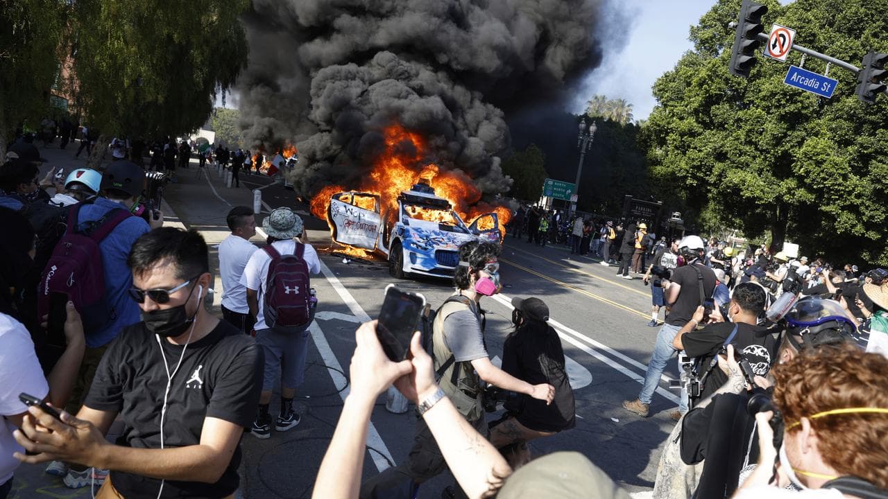 People watch cars burn in downtown Los Angeles
