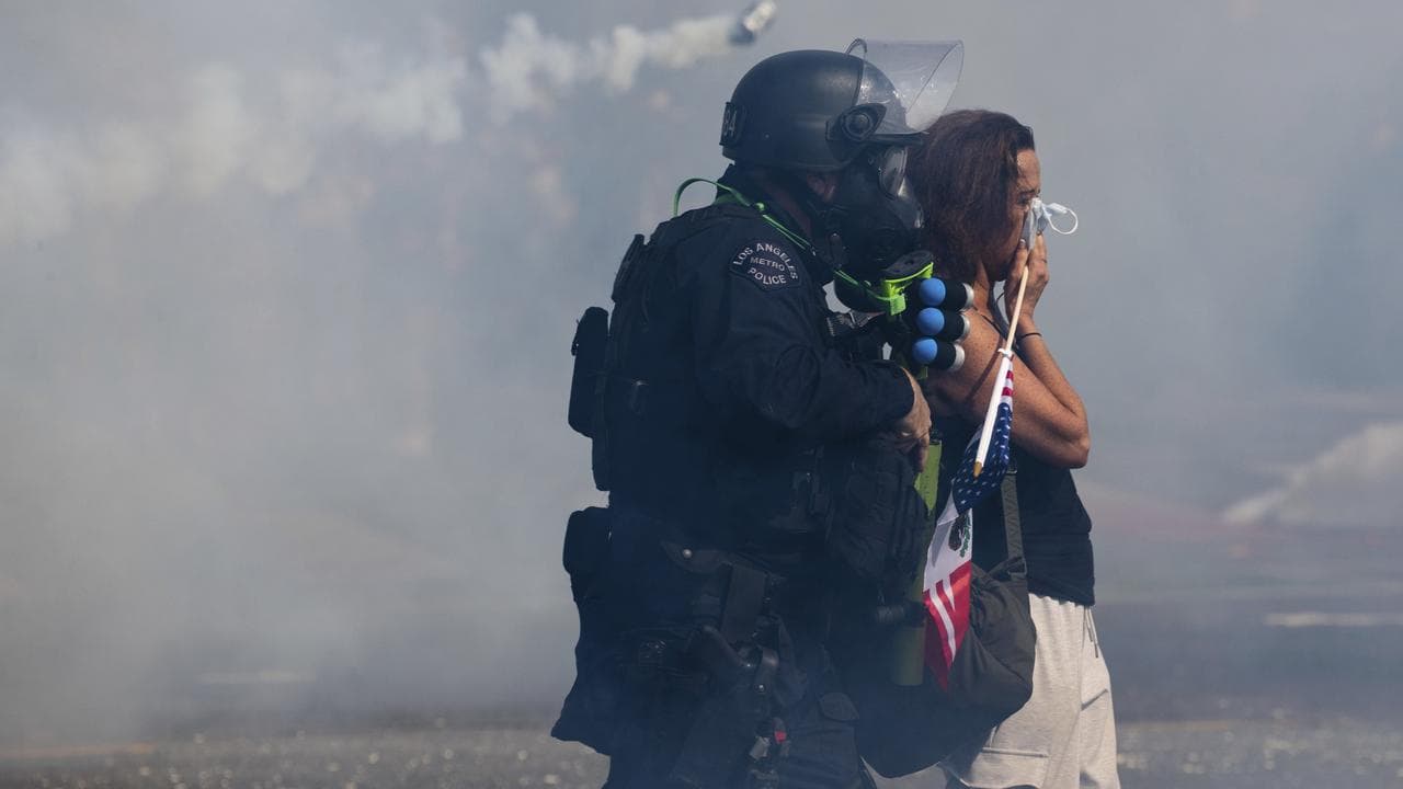 Police escort a protester as tear gas surrounds people