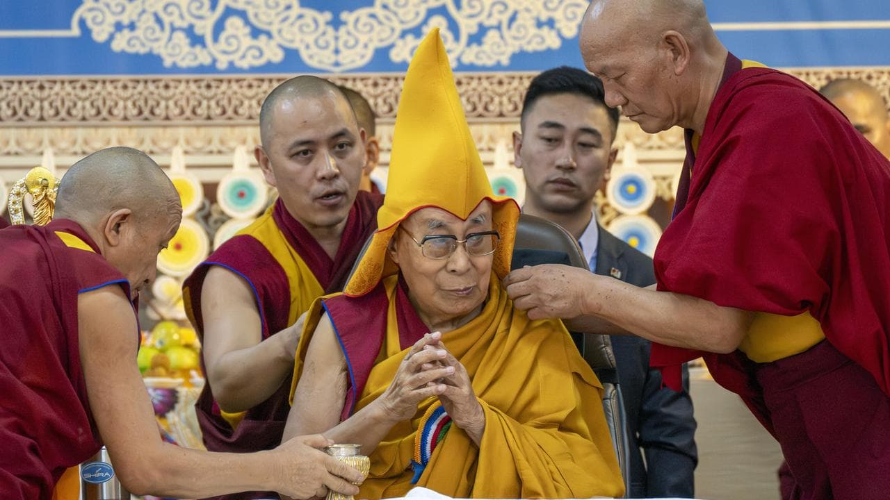 Monks help the Dalai Lama wear a ceremonial hat in Dharamshala, India