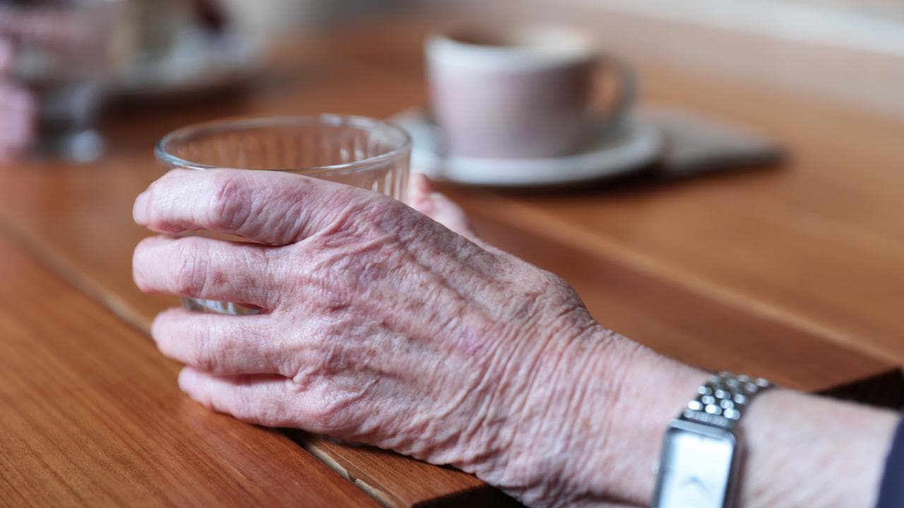 An elderly person holds a cup
