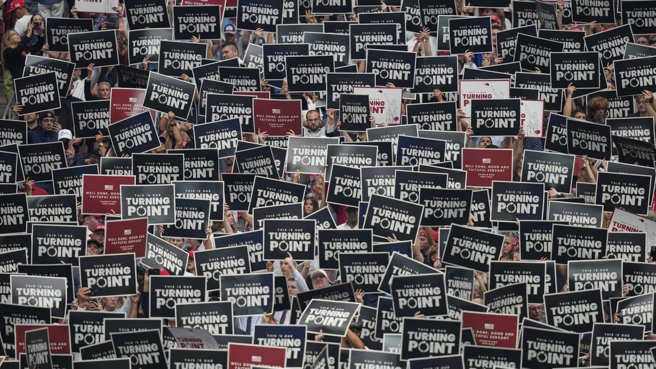 People hold up signs during the memorial for Charlie Kirk