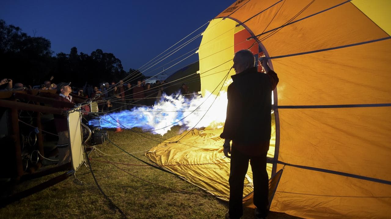 A photo of a pilot filling a hot air balloon at dawn.
