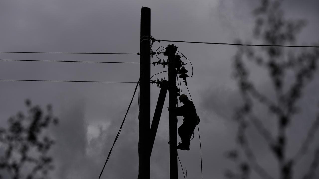 A worker climbs a utility pole while repairing power lines