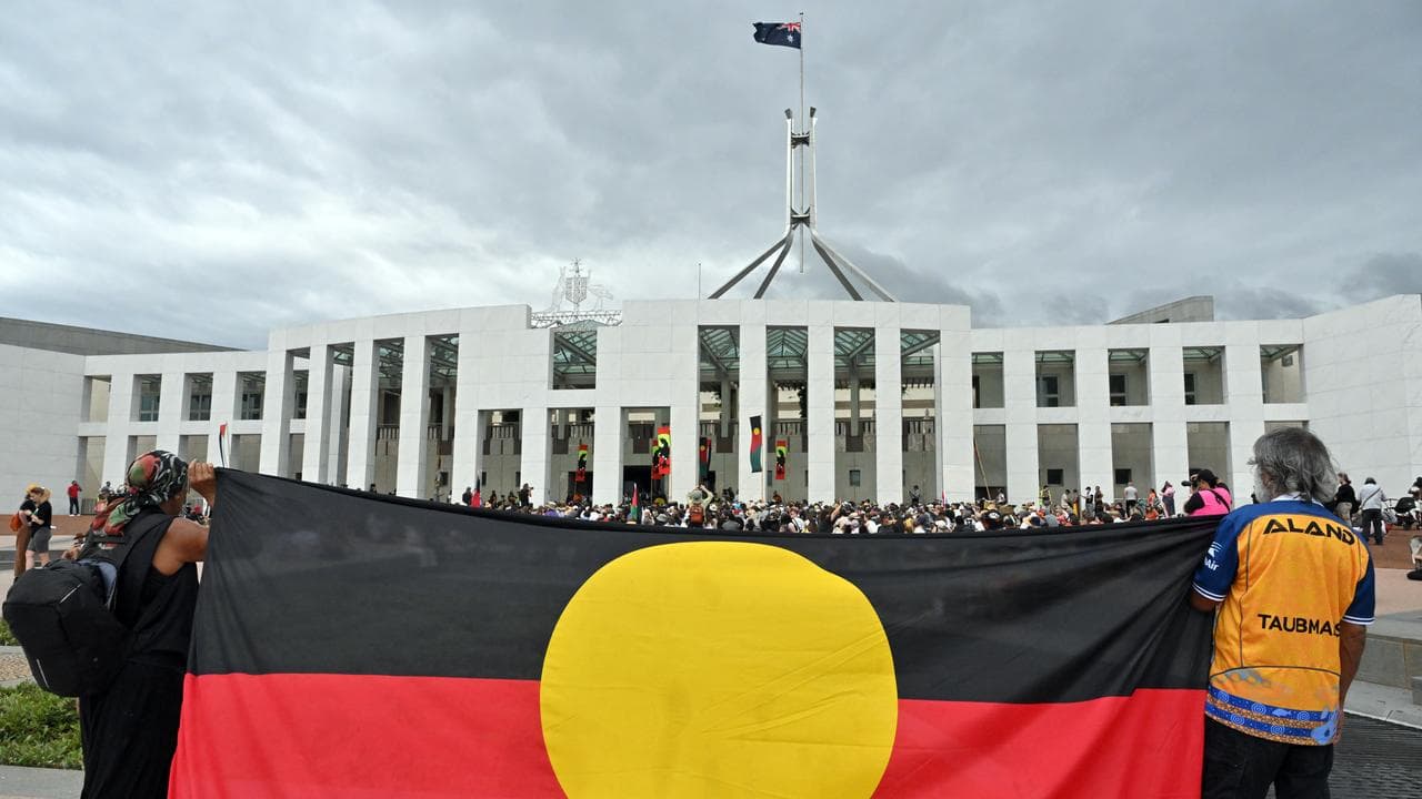 Protesters hold the Aboriginal flag at Parliament House in Canberra