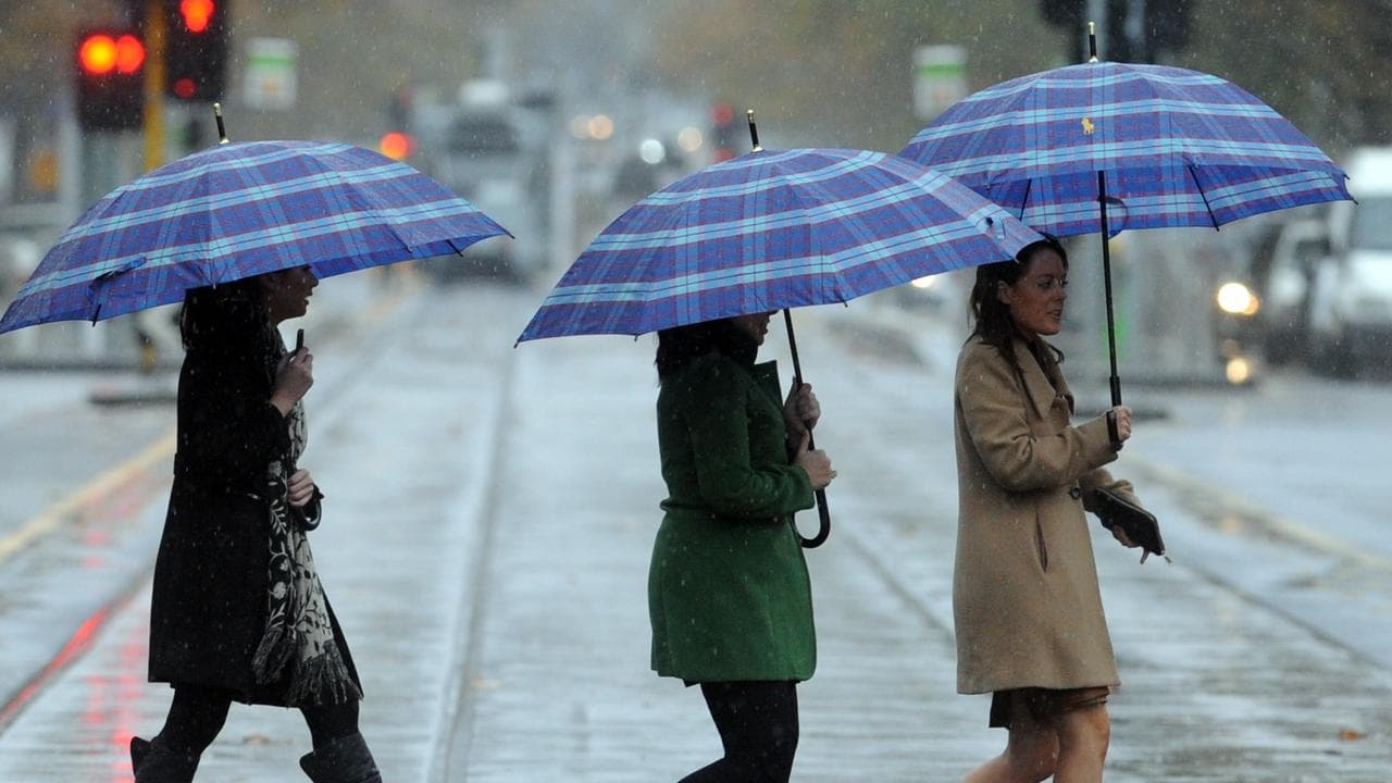 Three women cross St. Kilda Road amid wind and rain
