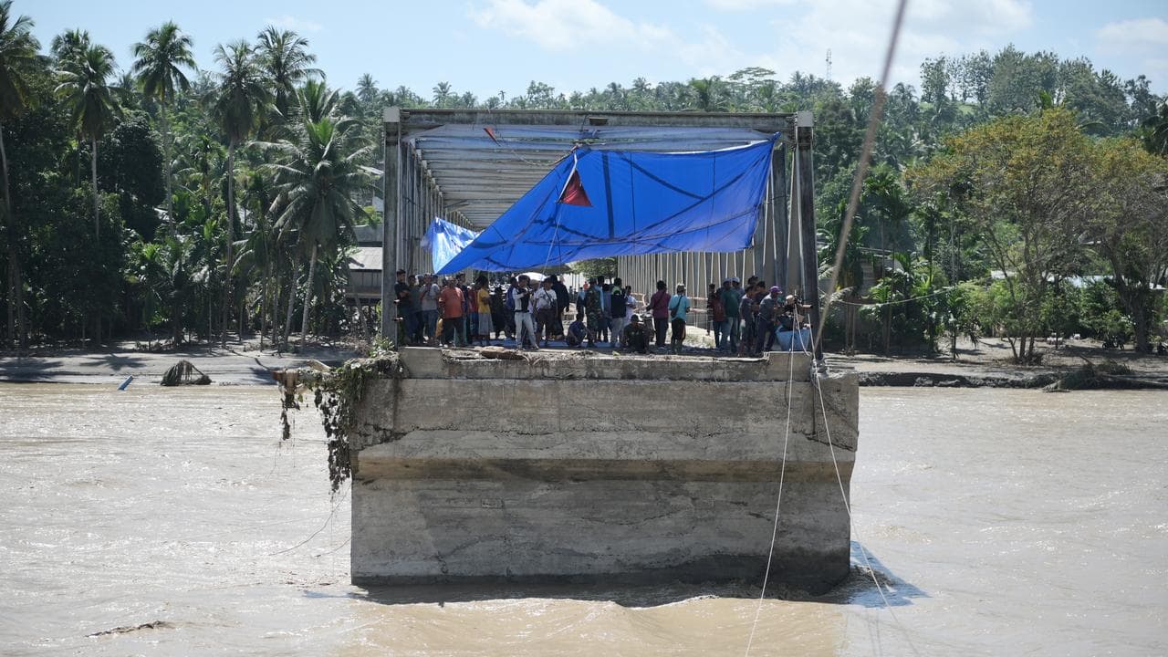 People stand on a bridge heavily damaged in a flash flood