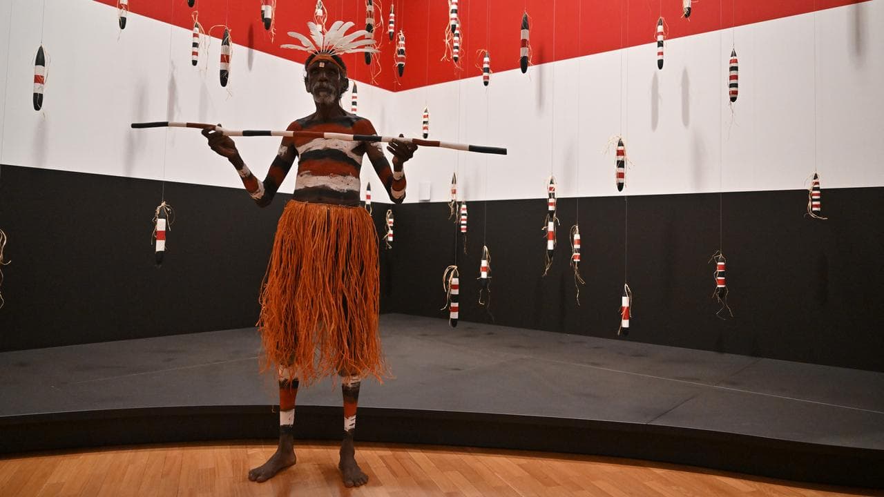 An indigenous dancer poses in front of an art installation