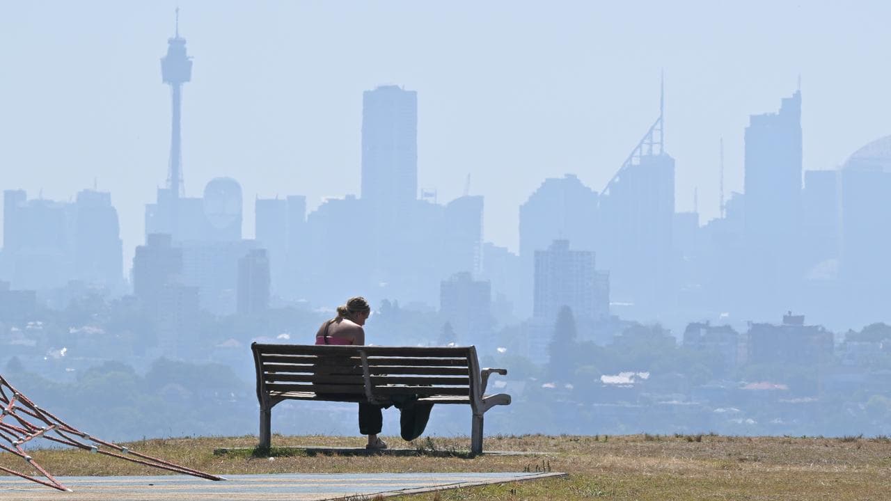 A woman on a park bench overlooking Sydney blanketed by smoke haze