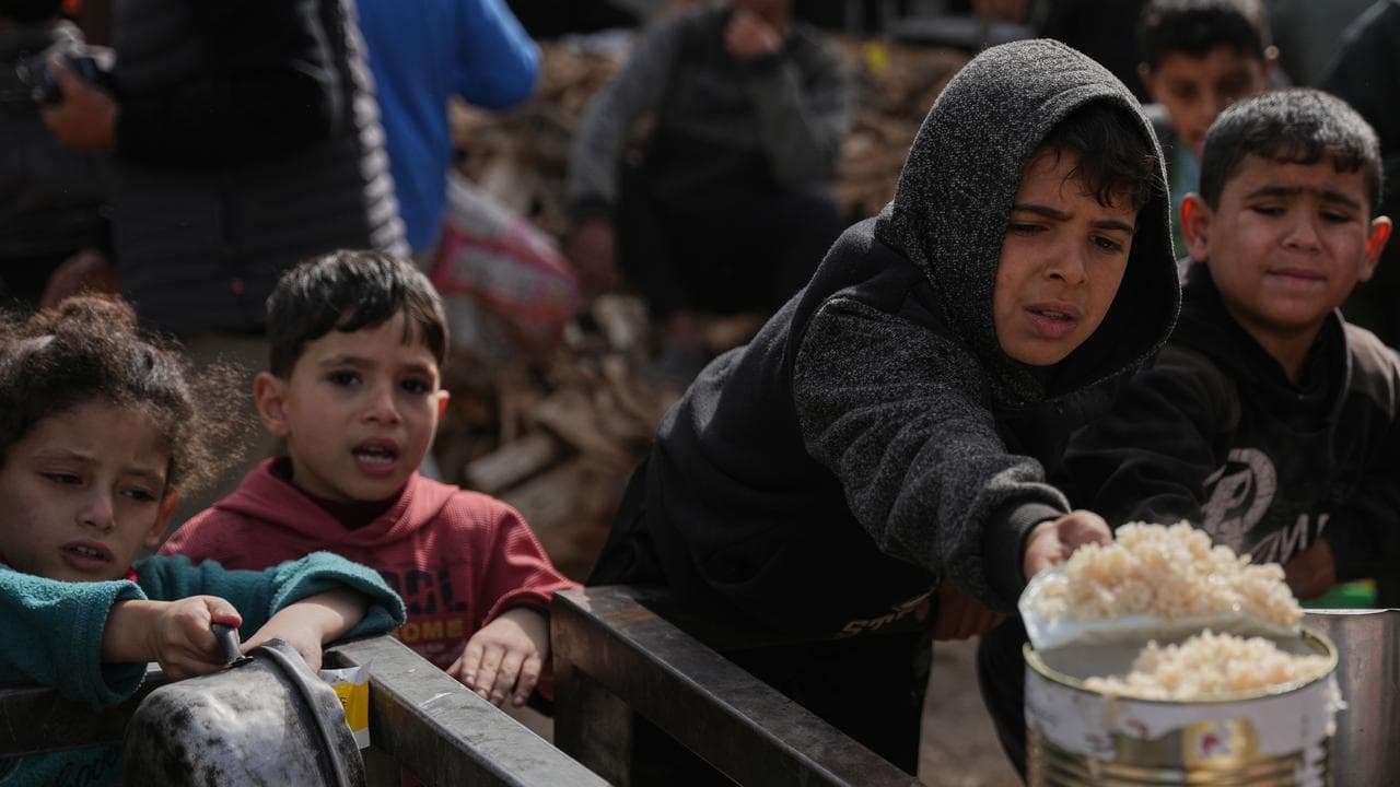 Palestinian children receive food at a community kitchen in Nuseirat