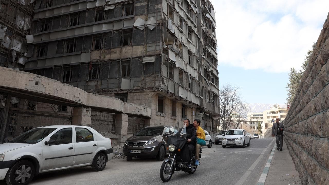 People drive past the destroyed Gandhi hospital in Tehran