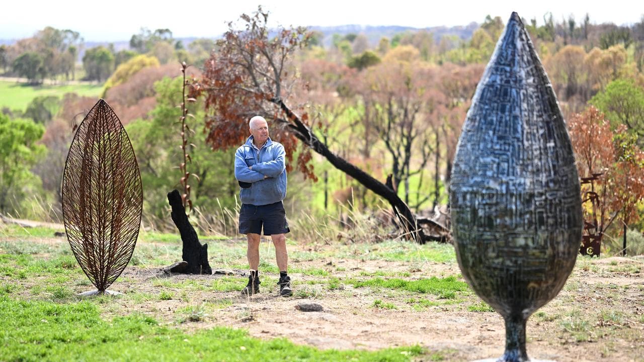 A man stands outdoors, beside some of his scrap-metal scultures.