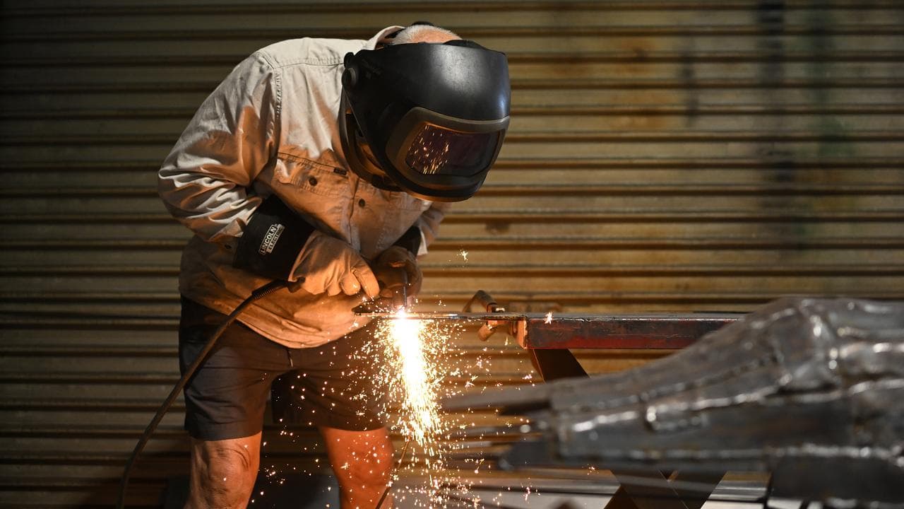 An artist wears a mask while welding scrap metal in a workshop.